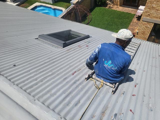 Crew member coating a corrugated roof