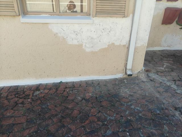 Damaged plaster at the base of a wall next to a downpipe