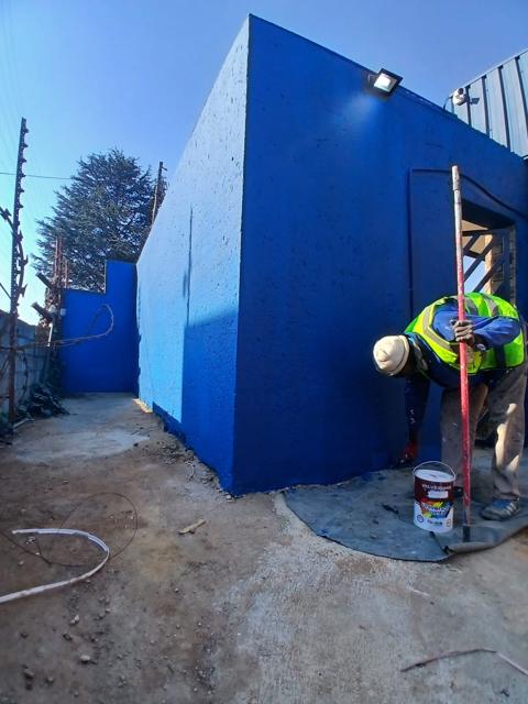 Crew member in hi-vis painting industrial walls blue