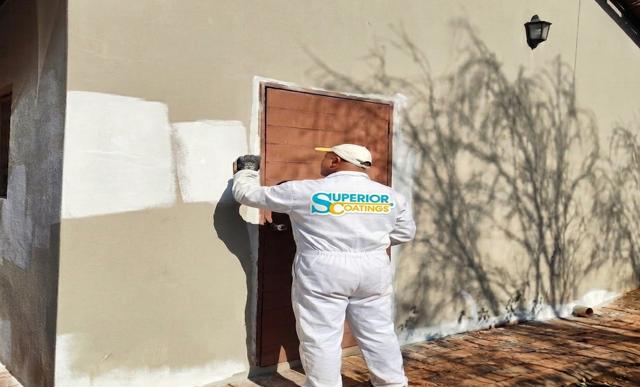 Painter in Superior Coatings overalls cutting in around a door